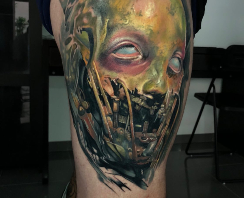 Tatuaje de un zombie con una cara terrorífica que tiene una maquina en la boca