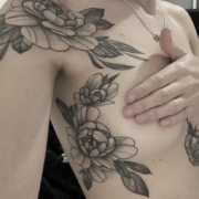 Tatuaje de peonias lineales con sombreado suave en puntillismo en el hombro y alrededor del pecho.