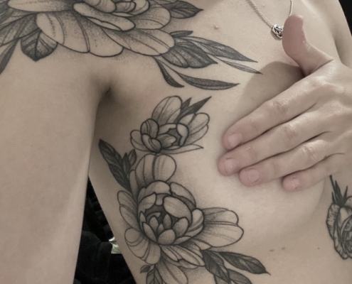 Tatuaje de peonias lineales con sombreado suave en puntillismo en el hombro y alrededor del pecho.