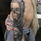 Tatuaje en el brazo de una mujer de una calavera con corona de espinas y un rostro de mujer terrorífico con detalles biomechanicos.