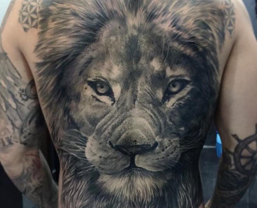 Tatuaje grande en la espalda de un hombre del rostro de un leon realista.