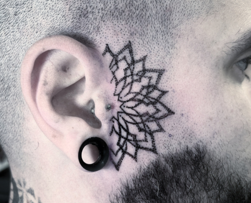 Tatuaje en la cara al lado de la oreja de medio mandala en pintillismo