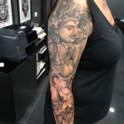 Tatuaje en el brazo de una mujer de una composicion de un dios Hindu con flores de cerezo.
