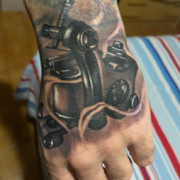 Tatuaje realista en la mano de una maquina de tatuar.