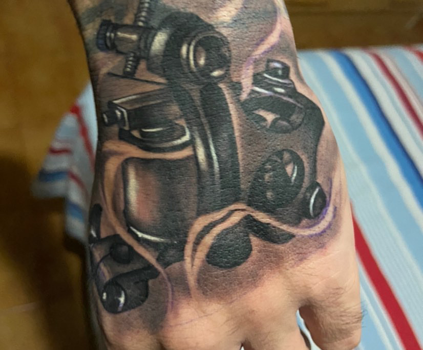 Tatuaje realista en la mano de una maquina de tatuar.