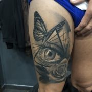 Tatuaje grande en un muslo de un ojo dentro de un triangulo decorado con una mariposa y una rosa.