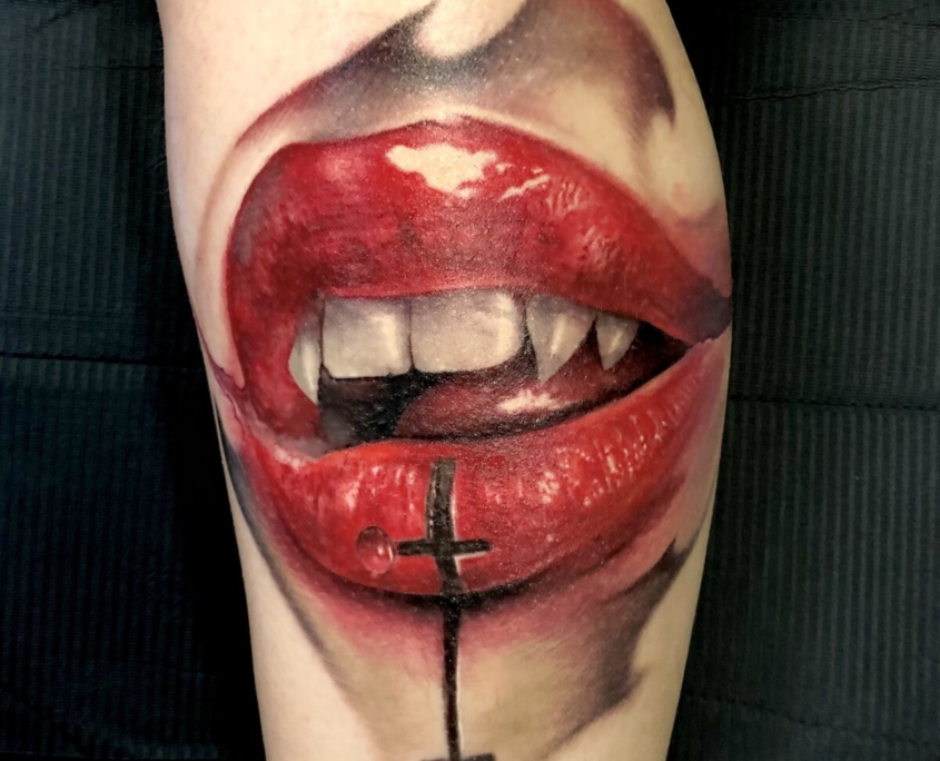 Tatuaje en el muslo de una boca de vampira sexy con una cruz invertida en el labio inferior.