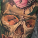 Tatuaje de una calavera realista a color con una mariposa y una rosa roja