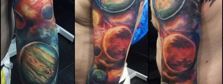 Tatuaje en el brazo de un hombre de una galaxia y planetas a color.