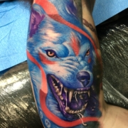 Tatuaje en el interior del biceps del lobo de la princesa mononoke de color azul con la boca abierta y expresion agresiva.