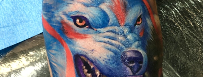 Tatuaje en el interior del biceps del lobo de la princesa mononoke de color azul con la boca abierta y expresion agresiva.