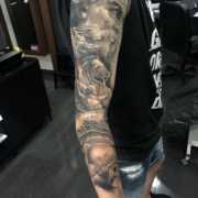 Brazo de hombre tatuado en estilo realista negro y grises con una tematica de dioses Griegos.