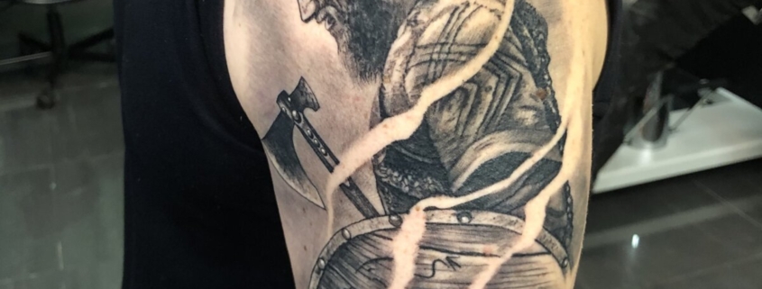 Tatuaje de Ragnar de Vikingos con un hacha y escudo.