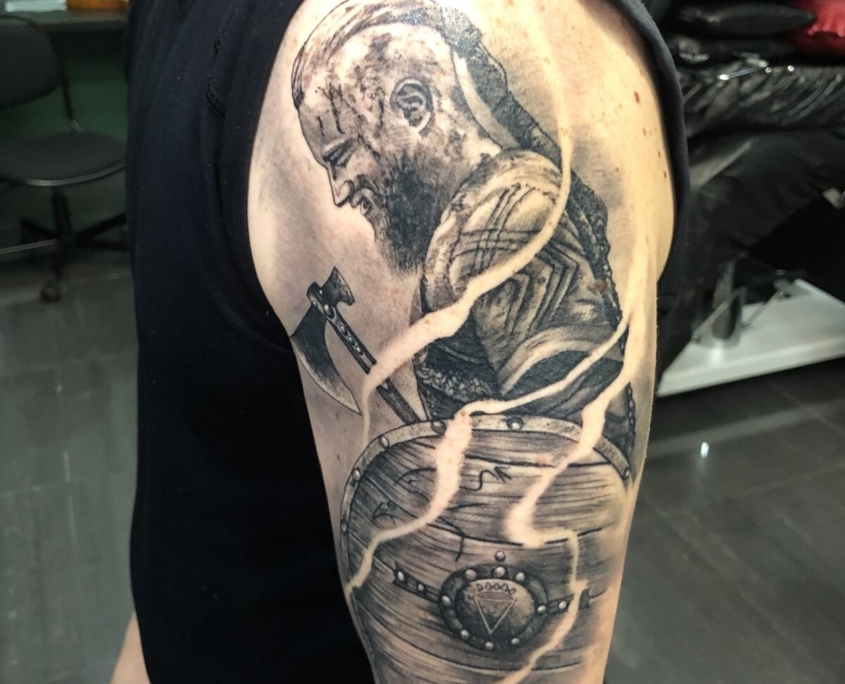 Tatuaje de Ragnar de Vikingos con un hacha y escudo.