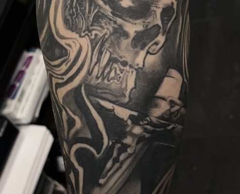Tatuaje en el brazo de una calavera con un grabado de los clavos de Cristo, agarrando una cruz.