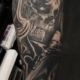 Tatuaje en el brazo de una calavera con un grabado de los clavos de Cristo, agarrando una cruz.