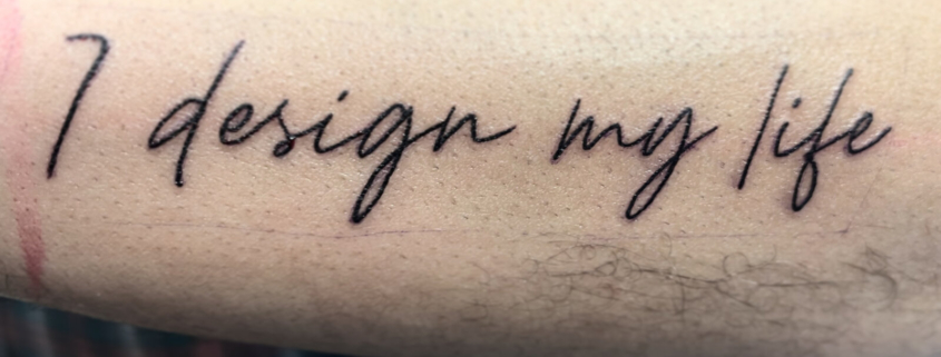 Tatuaje de la frase: I design my life, en una linea fina y elegante.